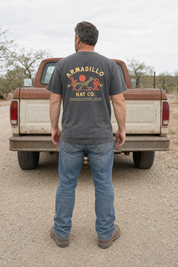 Man standing behind a weathered pickup truck wearing the Roadrunner Tee in Pepper charcoal, full back print visible with Streams in the Desert, Isaiah 35:6